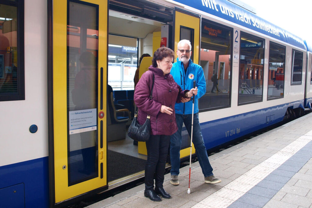 Mann erleichtert einer Dame den Ausstieg aus dem Zug